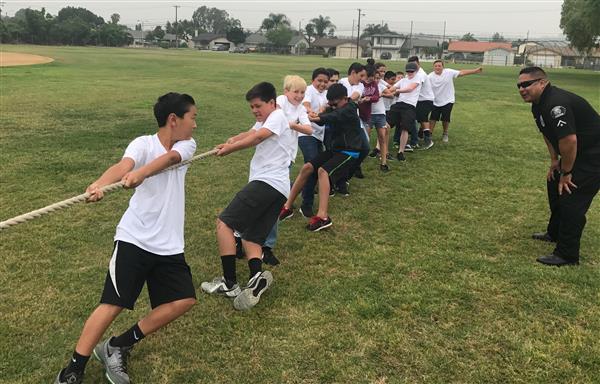 Several junior high age students play tug-of-war while a Chino Police Officer encourages them